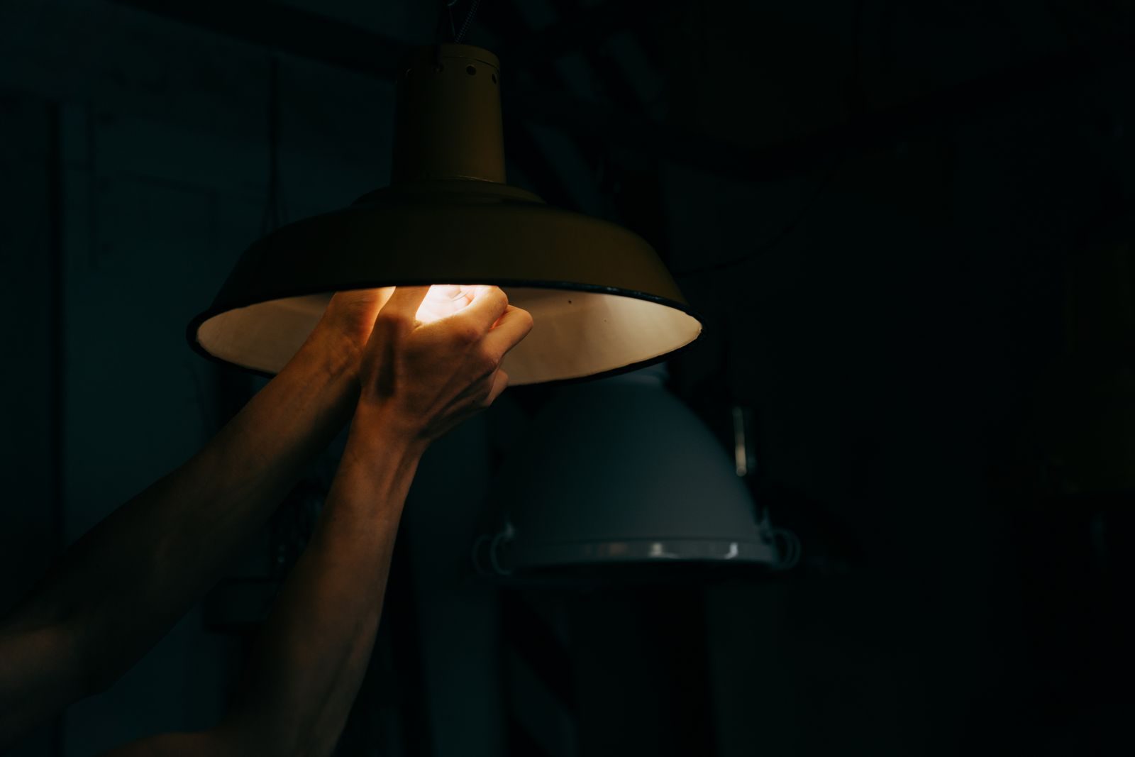 A person adjusts a vintage pendant lamp indoors, highlighting interior design and moody lighting.
