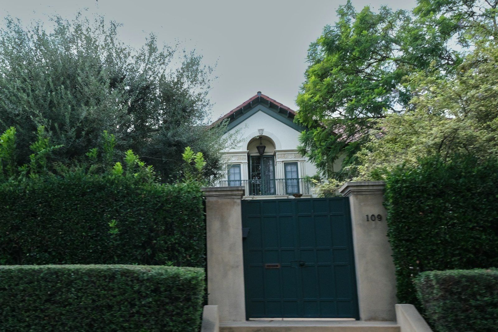 A white house with green gate surrounded by trees
