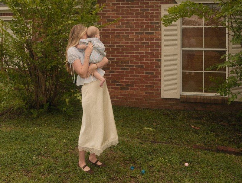 Mother holding baby outdoors near a brick house